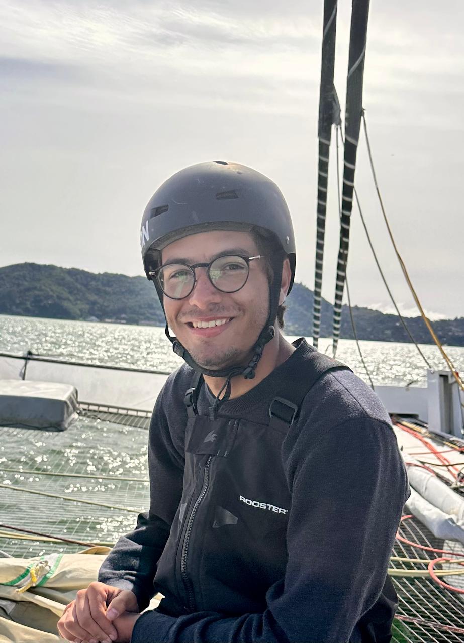 Julio Cesar Avellar sentado a bordo, usando capacete, óculos e colete de vela