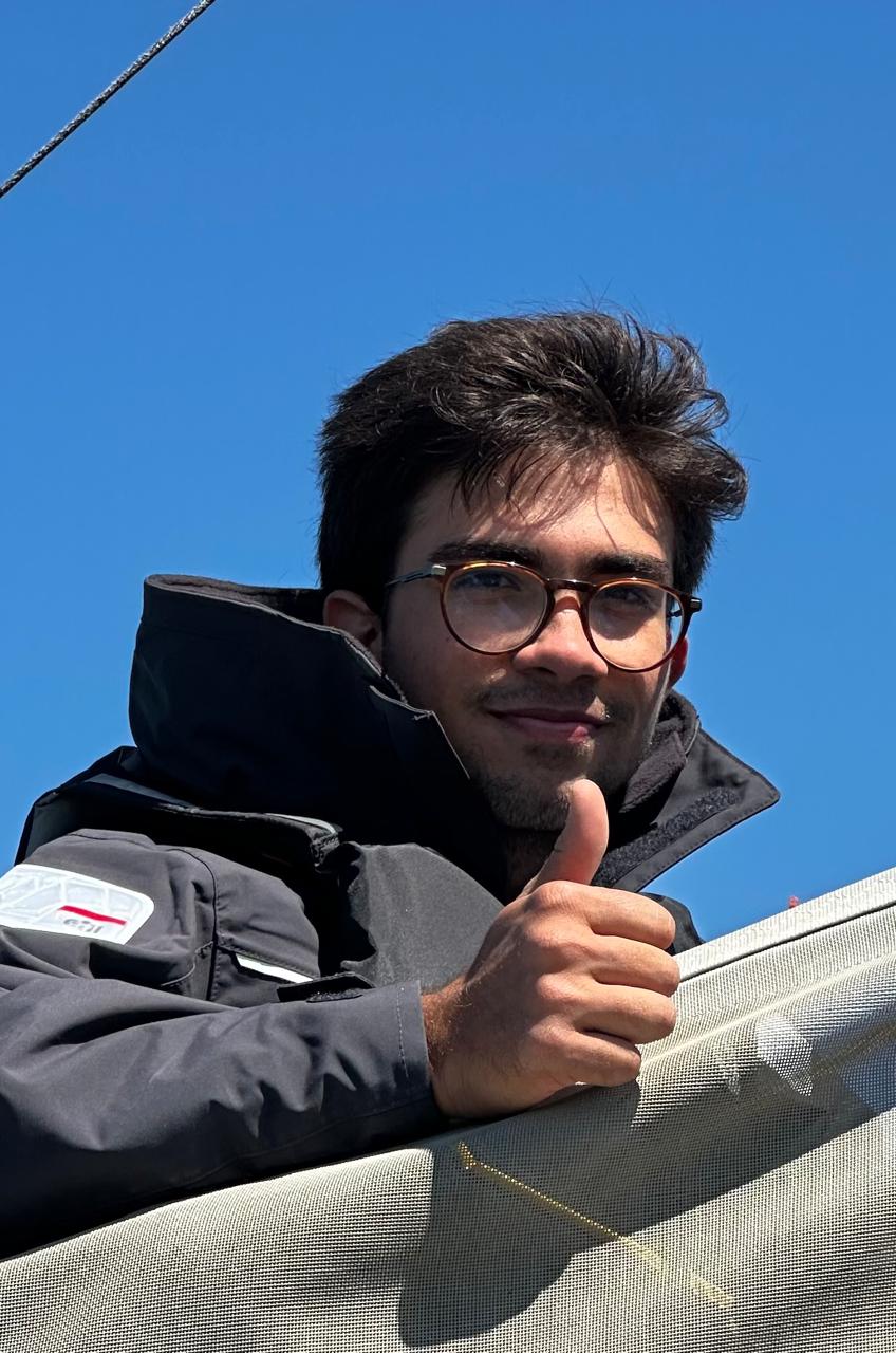João Pedro Cardoso de óculos, com céu azul ao fundo, fazendo sinal positivo com o polegar